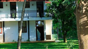 Un edificio de dos pisos con balcón, entrada empavedada y patio con césped.