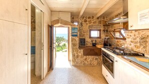 A kitchen with stone walls, wooden cabinets, and a view of the sea.