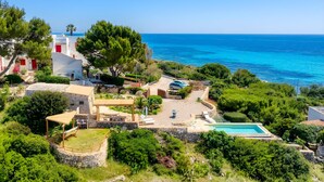 A coastal property with a swimming pool, a covered outdoor seating area, and a view of the sea.