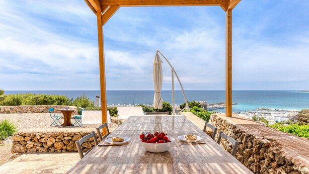 A wooden pergola with a table set for two, overlooking a coastal view.
