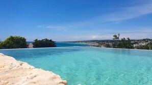 A clear blue infinity pool with a view of a distant beach and town.