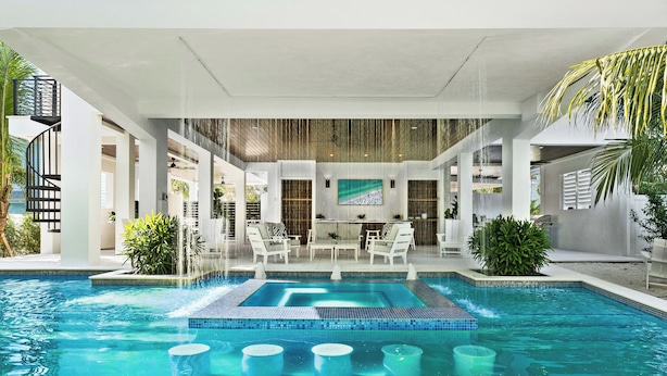 Un espace piscine intérieur moderne, doté d’un espace de détente central, entouré de chaises longues et agrémenté d’une cascade.