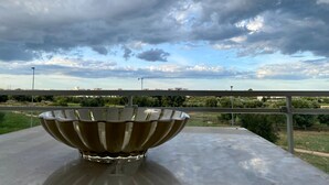 Un grand saladier métallique est posé sur une table, offrant une vue sur un ciel nuageux et des bâtiments éloignés.