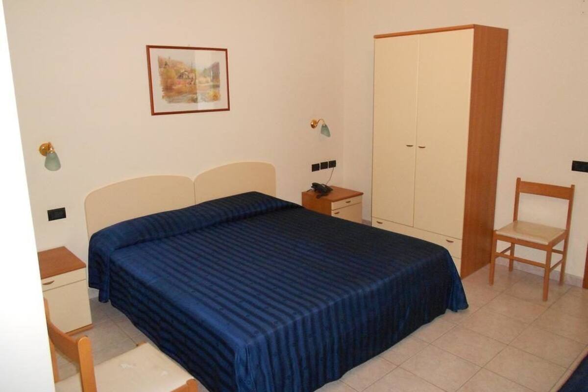 A bedroom with a bed, a wardrobe, a chair, a bedside table, and a wall-mounted lamp.