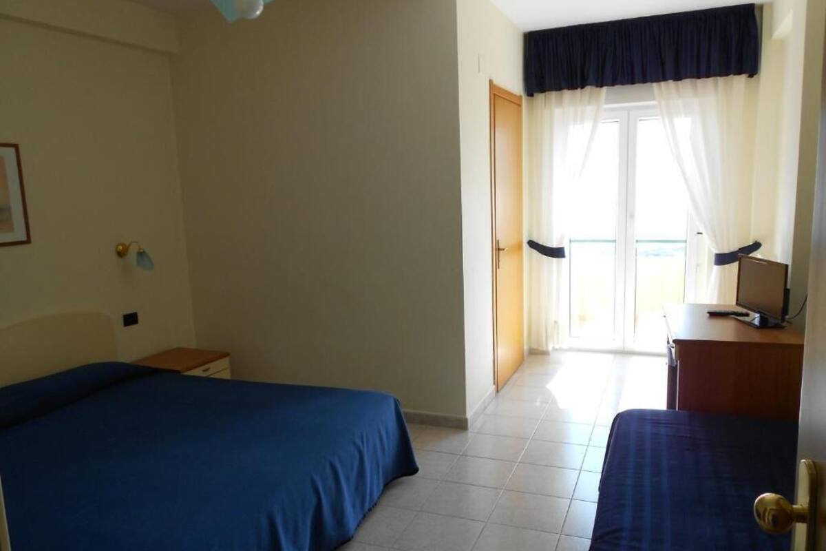 A hotel room with two beds, a desk, a chair, a lamp, and a view of the outside.