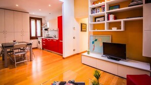 A modern living room with a flat-screen TV, a dining area with a table and chairs, and a kitchen with red cabinets. - Ca’ Lunetta  (Venezia)