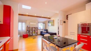 A modern apartment with a dining area, a living room with a sofa, and a kitchen with red cabinets. - Ca’ Lunetta  (Venezia)