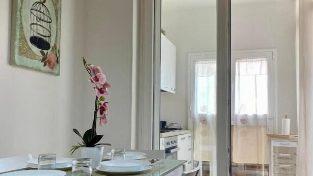A dining area with a glass table, white chairs, and a painting on the wall.