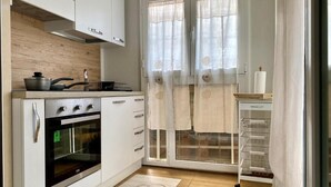 A modern kitchen with white cabinets, a built-in oven, a stove, and a window with sheer curtains.