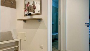 A hallway with a white bench, a mirror with a wooden frame, and a door leading to a bathroom.