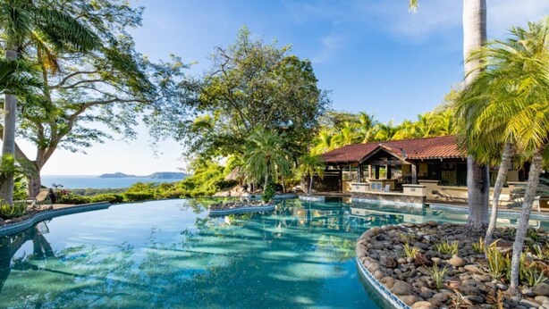 Ein Resort mit einem großen Infinity-Pool, umgeben von tropischer Vegetation und Blick auf den Ozean.