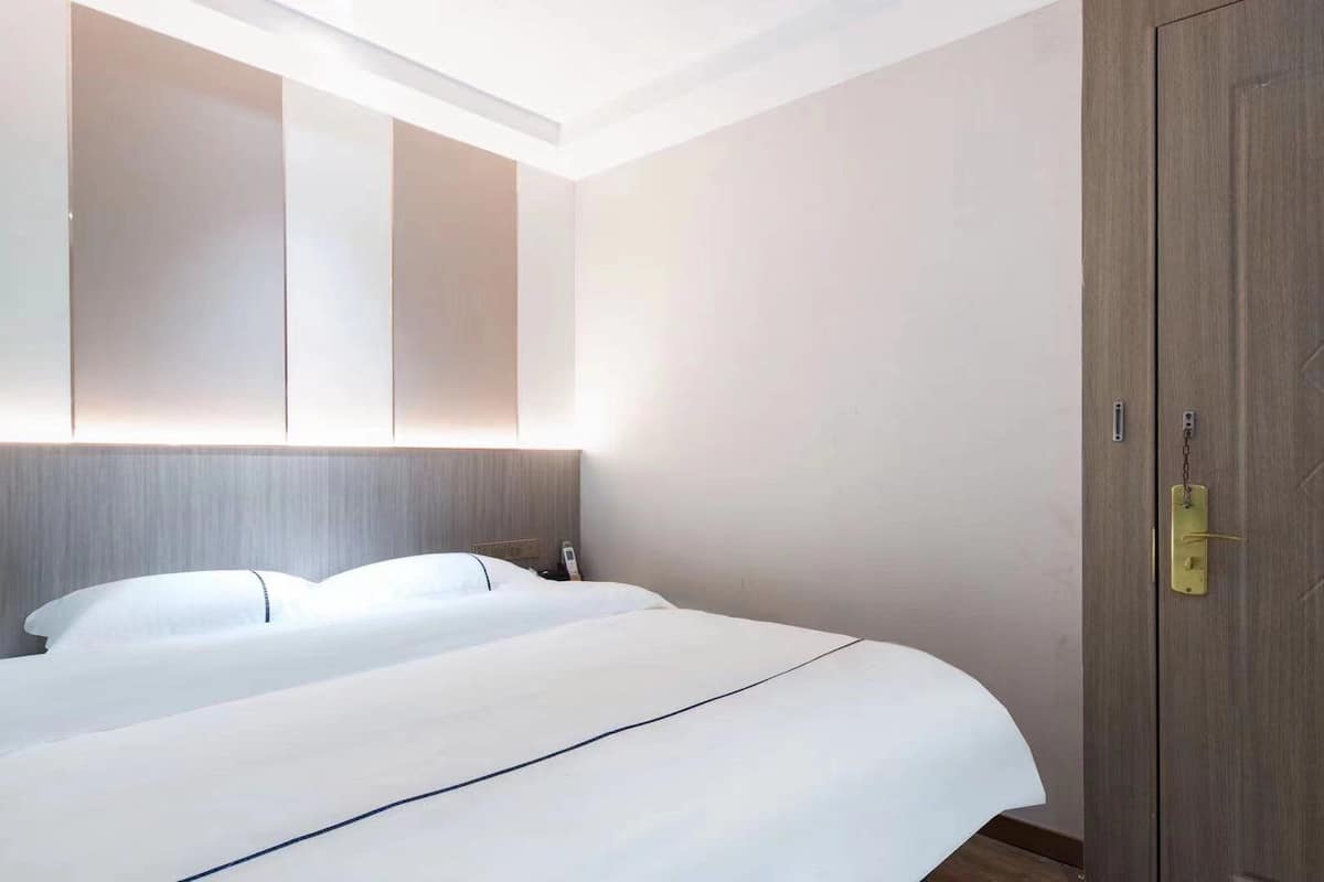 A hotel room with a large bed, a wooden wardrobe, and a wall-mounted light fixture.