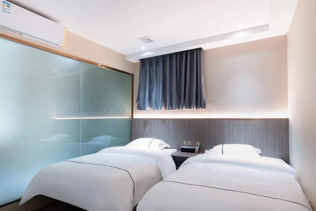 A hotel room with two beds, a glass partition, a dark curtain, and a bedside table with a phone.