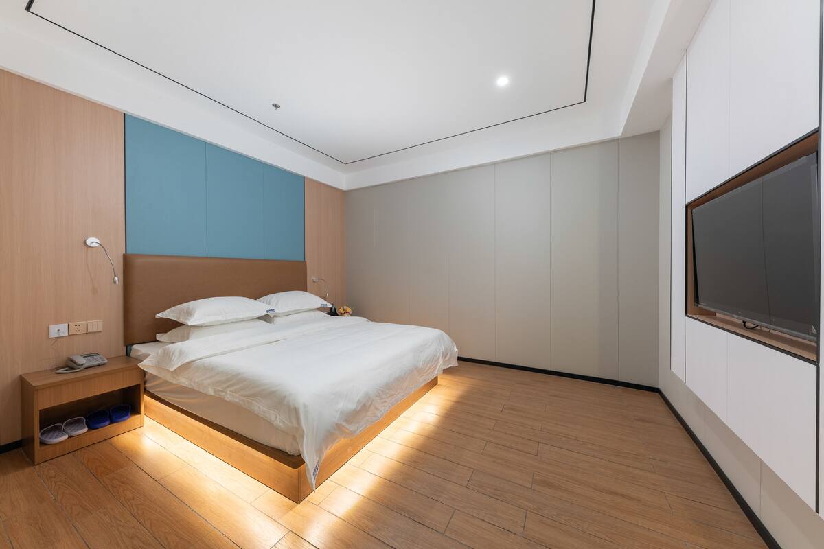 A modern bedroom with a bed, bedside table, and a TV mounted on the wall.