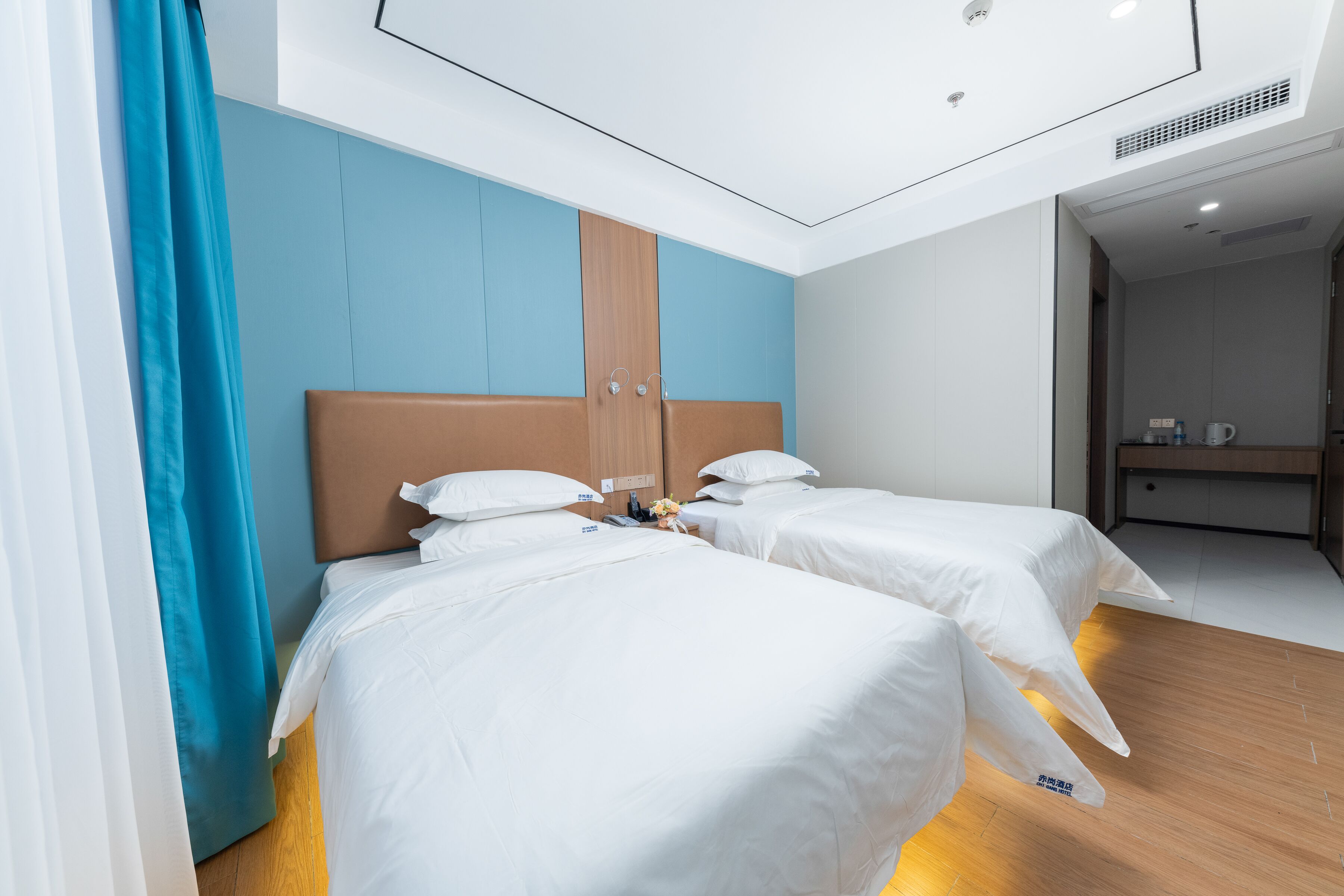 Ein Hotelzimmer mit zwei Betten, einem Holzkopfende und einer blauen Akzentwand.