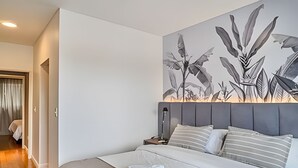 Ein Hotelzimmer mit einem großen Bett, einem Nachttisch, einer Lampe und einem Wandbild mit Pflanzen.