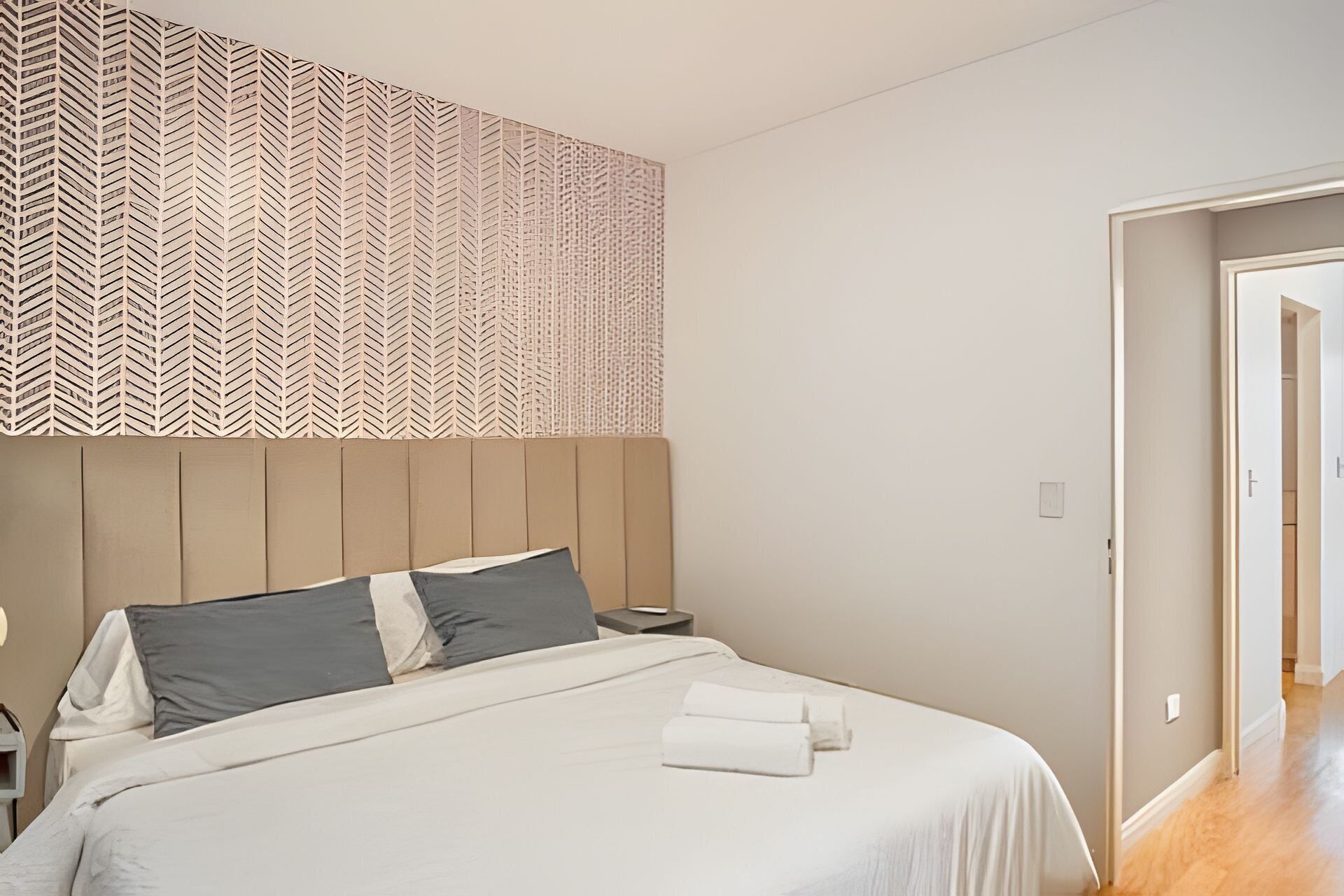 A bedroom with a bed, pillows, a nightstand, and a wall with a patterned design.