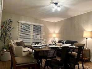 Un coin repas avec une table dressée pour quatre personnes, entourée de chaises, d’un canapé et d’une plante en pot.