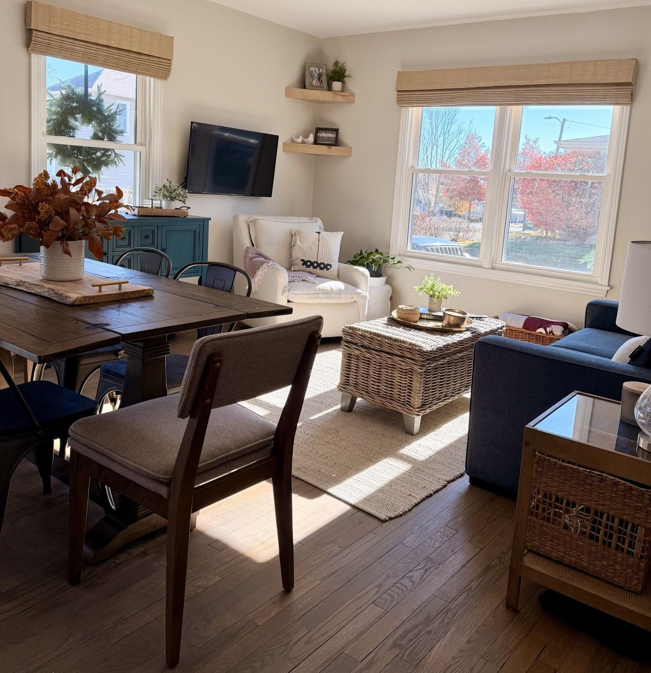 A living room with a dining table, chairs, a sofa, a TV, and a window with a view of trees.