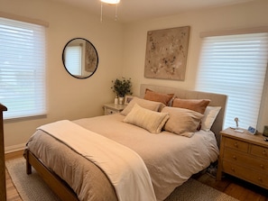 Une chambre à coucher avec un lit, des tables de chevet, un miroir et un tableau accroché au mur.
