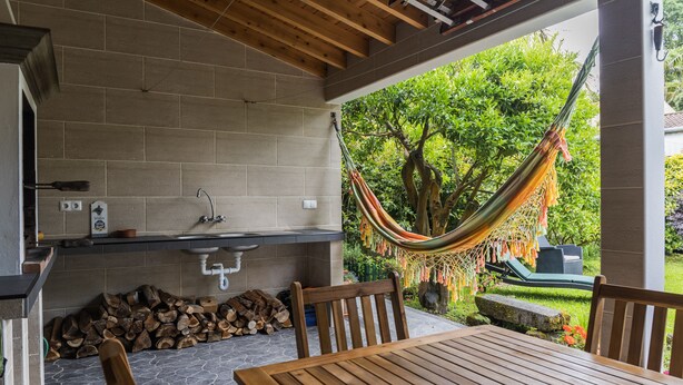 An outdoor patio with a wooden table and chairs, a hammock, and a stone wall. - Casa da Tia Luísa (Furnas)