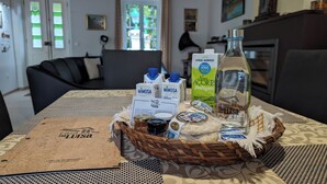 A dining table with a basket containing food items, a bottle of water, and a book titled 'Casa da Luísa'. - Casa da Tia Luísa (Furnas)