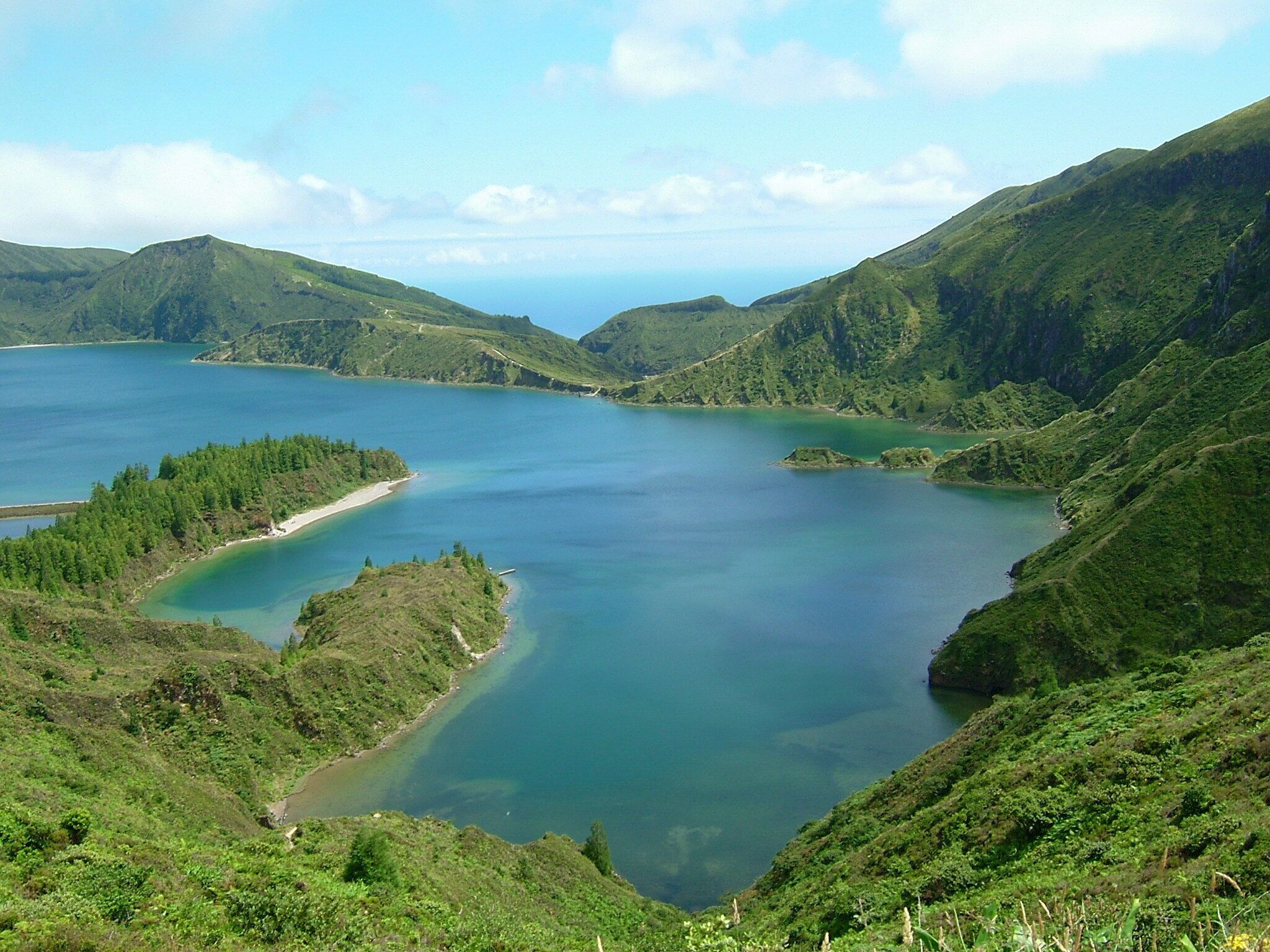 A panoramic view of a coastal landscape with a large body of water surrounded by lush green hills.