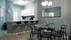 Cocina compacta con armarios blancos, una isla central con taburetes y un comedor con mesa redonda y sillas.