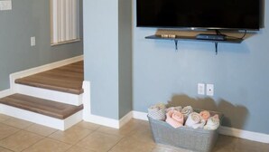 Una sala de estar con un televisor montado en la pared, una escalera de madera y una cesta con mantas dobladas en el suelo.