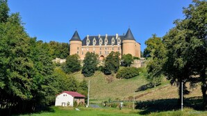 Eine große Burg mit mehreren Türmen, umgeben von üppiger Vegetation und einem kleinen weißen Gebäude im Vordergrund.