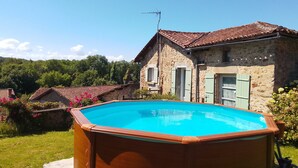 Ein hölzerner Pool mit einem Steinhaus im Hintergrund.