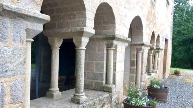 Ein Gebäude aus Stein mit Rundbogenfenstern und Säulen, Außenbereich mit Sitzgelegenheiten und Blumentöpfen.
