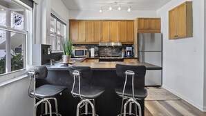 A modern kitchen with wooden cabinets, stainless steel appliances, and a bar area with stools.