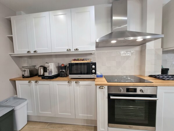 A modern kitchen with white cabinets, a stainless steel range hood, a built-in oven, and a coffee maker. - Le Magnolia | Terrace & Private Parking | Sleeps 6 (Honfleur)