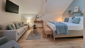 Een moderne slaapkamer met dakraam, een bed met blauwe deken, een sofa, een tafeltje en een tv aan de muur.