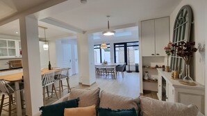 Een ruime woonkamer met een bank, een eettafel met stoelen en een keuken met kasten en een raam.