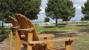 Una silla Adirondack de madera en un parque con césped y árboles al fondo.