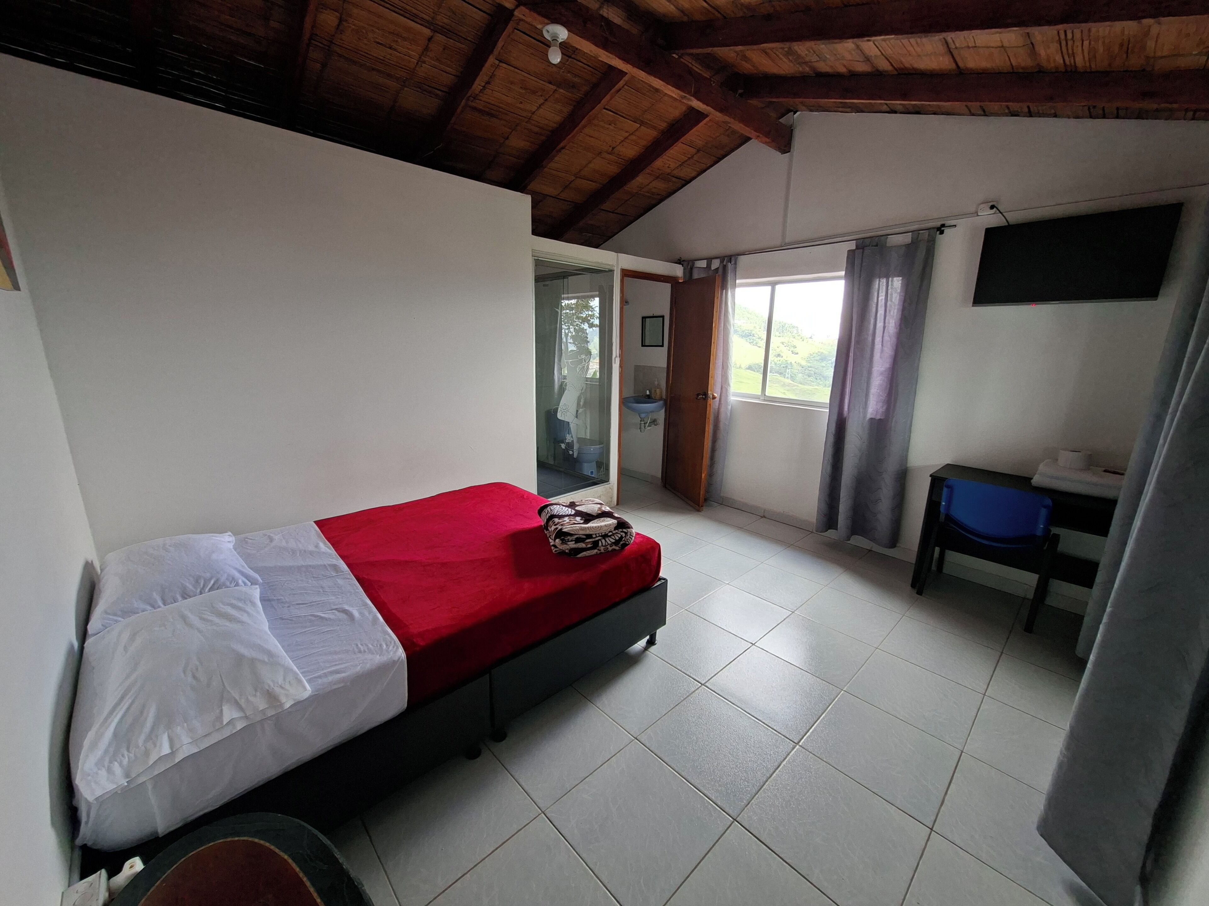 A room with a bed, a desk, a chair, a window with curtains, and a ceiling fan.