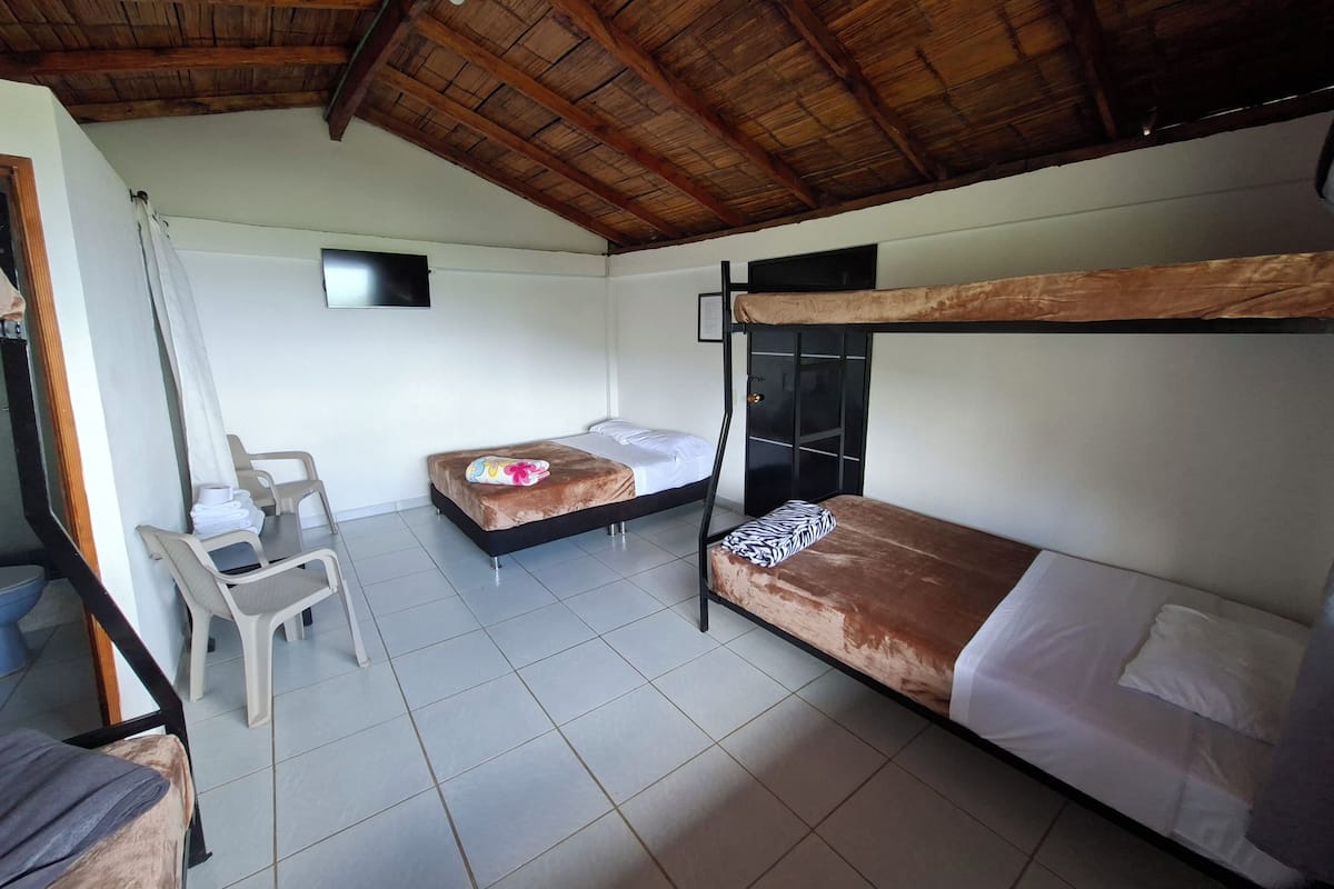 A room with two bunk beds, a desk with a chair, a small TV, and a tiled floor.