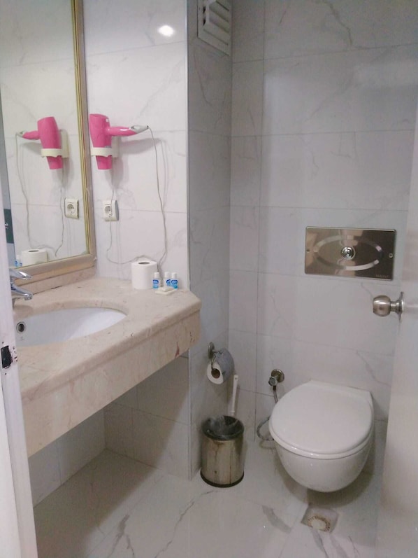Un baño con dos lavabos, inodoro, un cubo de basura y un espejo.