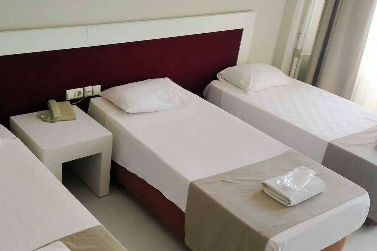 A hotel room with three single beds, a small bedside table with a telephone, and a window with curtains.