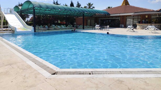 Una piscina con tobogán, sillas de descanso y una zona techada.