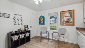 A room with a coffee bar, two patterned chairs, a ceiling fan, and a window with a view.