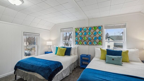 A bedroom with two beds, a skylight, a window, and a colorful abstract painting.