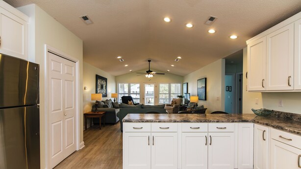 A modern kitchen with white cabinets, a stainless steel refrigerator, and a central island with a granite countertop. - The Ellis House:Pet Friendly Beach Home, 2 Screened Porches, Minutes to Beach Access (Edisto Beach)