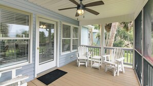 A covered porch with a ceiling fan, white chairs, and large windows with blinds. - The Ellis House:Pet Friendly Beach Home, 2 Screened Porches, Minutes to Beach Access (Edisto Beach)