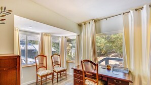 Una habitación con un escritorio de madera, dos sillas, un armario pequeño y una ventana con cortinas.
