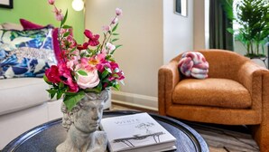A statue vase with flowers on a table, a book titled "WHITE" beside it, and a brown armchair in the background.