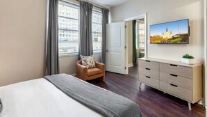 A hotel room with a bed, a chair, a dresser, and a TV on the wall. - Modern Elegance: 1BR Retreat with Rooftop Pool (New Orleans)
