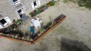Ein Luftbild eines Innenhofs mit einem runden Tisch und Stühlen, umgeben von erhöhten Blumenbeeten und einem Holz-Pflanzkasten.